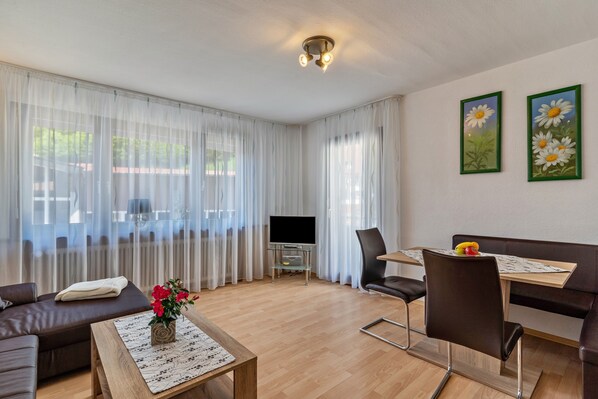 Un salon moderne comprenant un canapé, une table basse, une table à manger et des chaises. Un téléviseur à écran plat est posé sur un meuble, et deux tableaux encadrés ornent le mur.