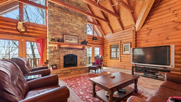 A log cabin interior with a stone fireplace, leather sofas, a flat-screen TV, and a red patterned rug. - Rustic mountain cabin with amazing view, pool table, jetted tub, W/D & fireplace (Boone)