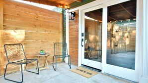 A wooden exterior wall, a sliding glass door, a metal chair, a small table with a plant, and a doormat.