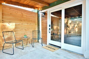 A wooden exterior wall, a sliding glass door, a metal chair, a small table with a plant, and a doormat.