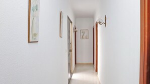 Um corredor estreito com paredes brancas, obras de arte emolduradas e uma porta que dá para outro quarto.