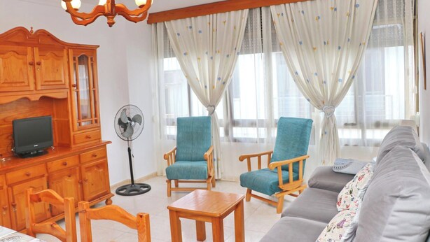Uma sala de estar com móveis de madeira, uma televisão, um ventilador e um sofá.