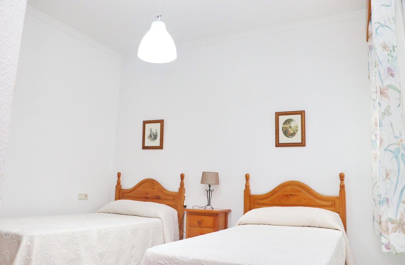 Ein Zimmer mit zwei Holzbetten, weißen Wänden und einer Deckenleuchte.