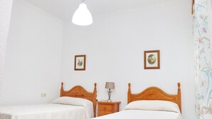 Quarto com duas camas de madeira, paredes brancas e um lustre.