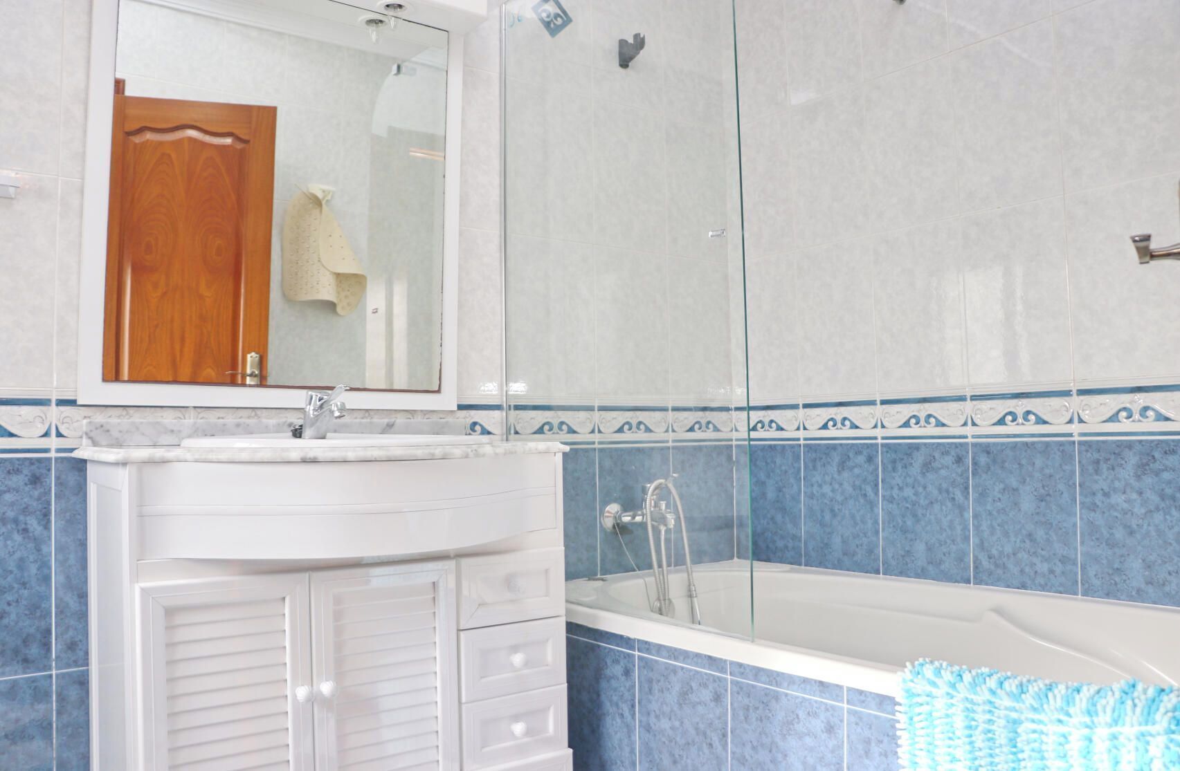 Un baño con un lavabo blanco, un espejo, una ducha y paredes con azulejos azules.