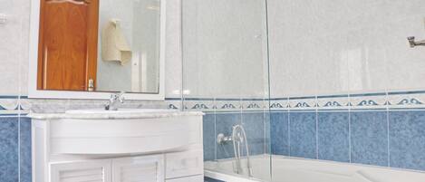 Un baño con un lavabo blanco, un espejo, una ducha y paredes con azulejos azules.
