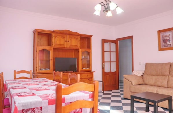 A living room with a sofa, a TV, wooden cabinets, and a dining area with a table and chairs.