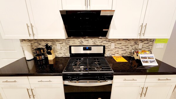 A kitchen with white cabinets, a black countertop, and a stainless steel stove.