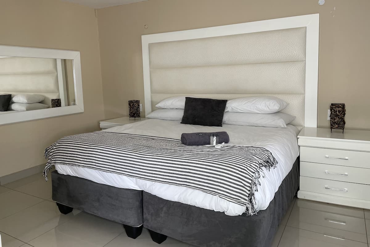 A modern bedroom with a large bed, a bedside table, a mirror, and a dresser.