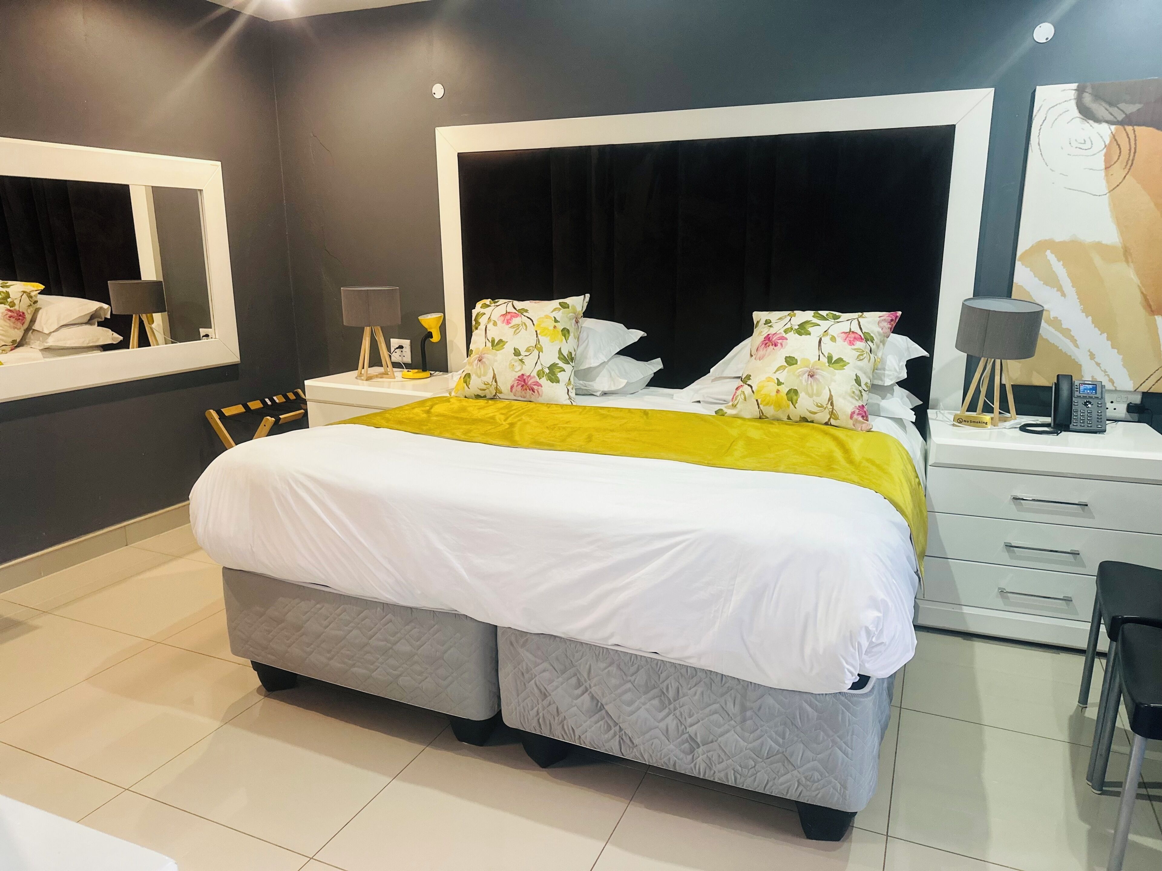 A modern bedroom with a large bed, bedside tables, a mirror, and a desk with a phone.