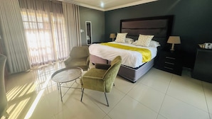 A hotel room with a bed, a chair, a small table, a nightstand, and a mirror. - 1 Oak lodge (Thulamela)