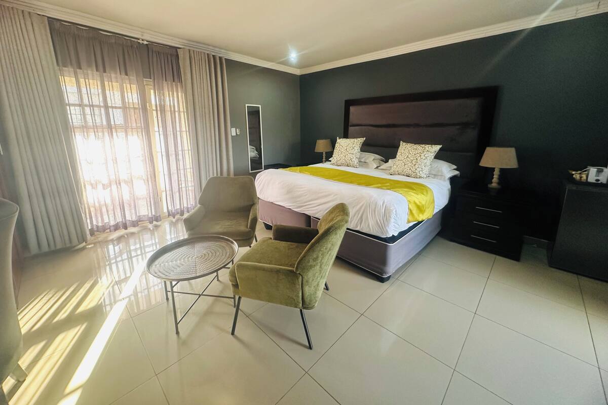 A hotel room with a bed, a chair, a small table, a nightstand, and a mirror.