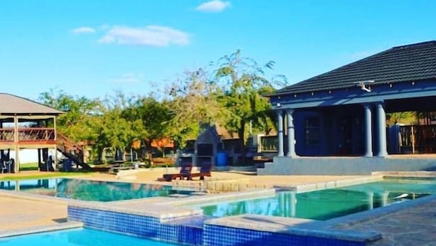 A swimming pool with clear blue water, surrounded by lounge chairs and a covered pavilion. - 1 Oak lodge (Thulamela)