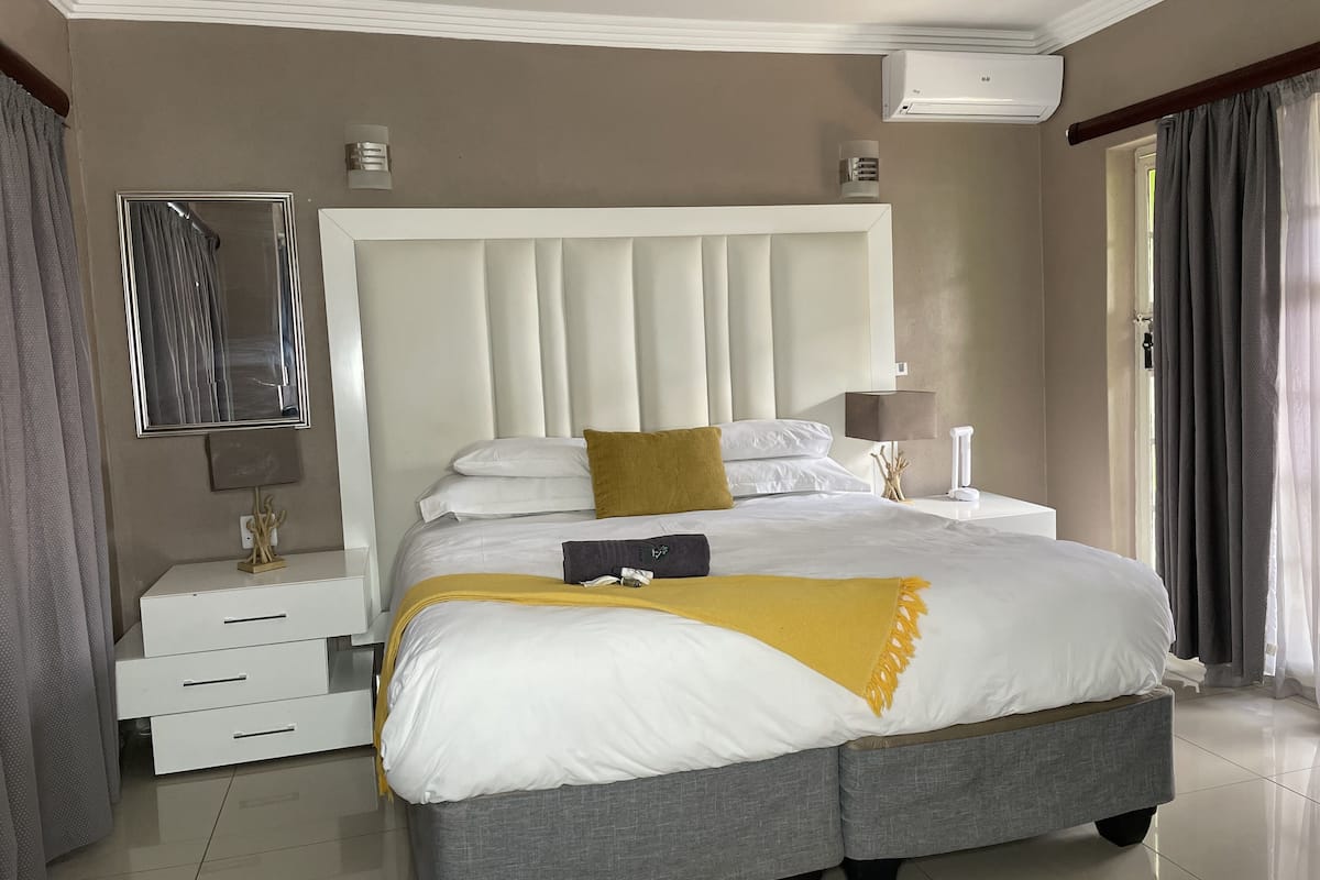 A bedroom with a large bed, bedside tables, a mirror, and an air conditioning unit.