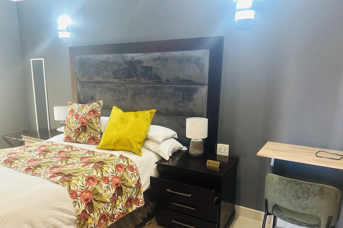 A hotel room with a bed, nightstands, a lamp, a chair, and a desk.