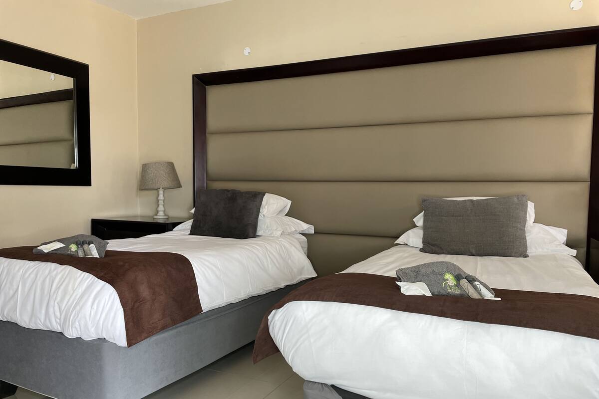 A hotel room with two beds, a nightstand, a lamp, and a mirror.