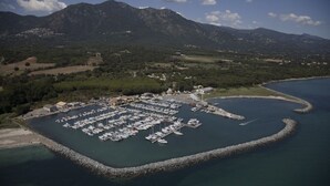 An aerial view of a marina surrounded by mountains, with boats docked and a small building nearby. - Appartement 2 Piscines, 100m de la Mer, 4/6 Personnes (Santa-Maria-Poggio)