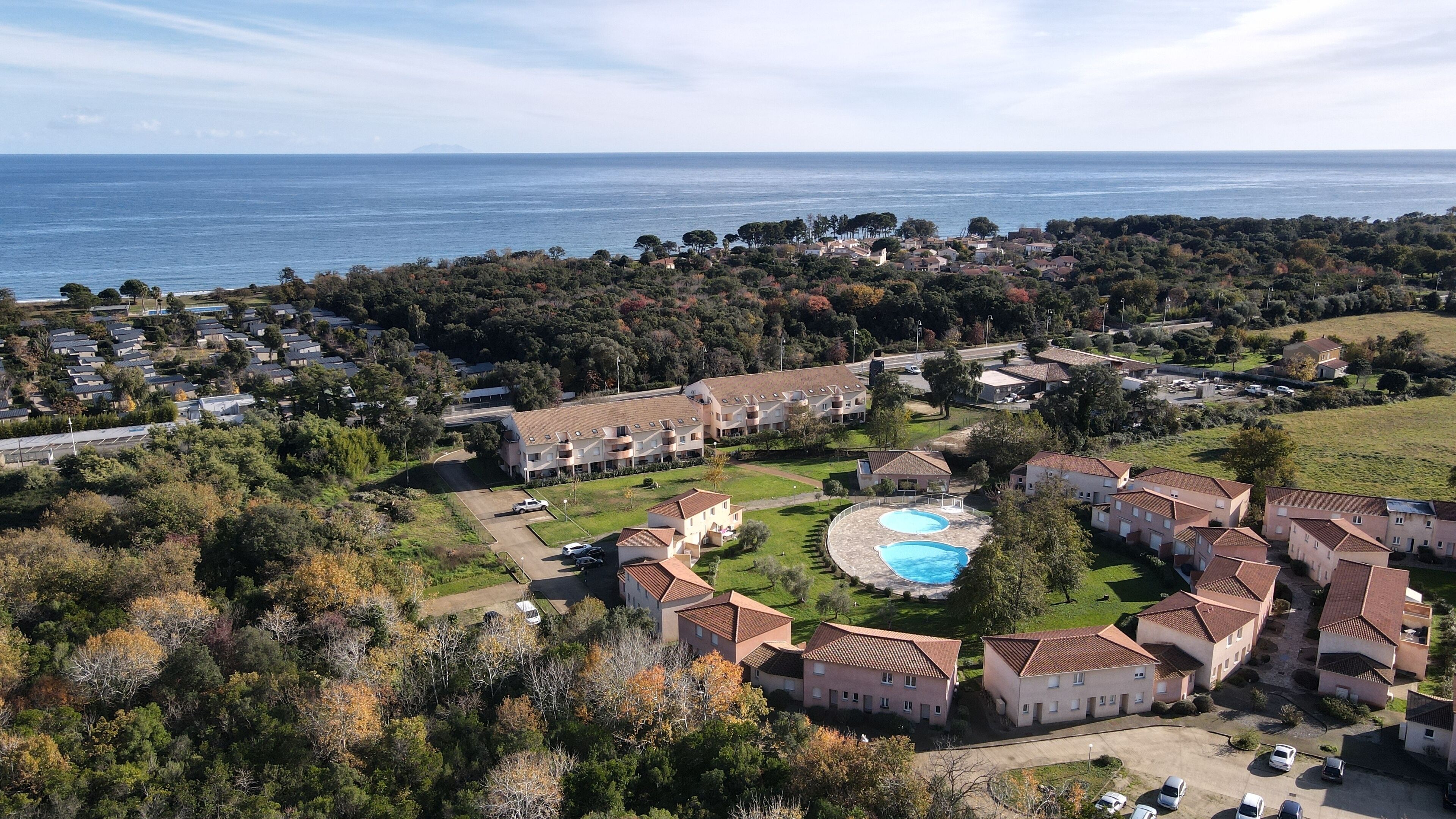 Vue aérienne d’un quartier résidentiel situé sur la côte, avec de nombreux immeubles d’appartements, une piscine et une vue sur la mer.