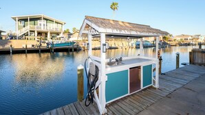 Um barco atracado com um pequeno espaço de bar, um deck de madeira e uma casa ao fundo.
