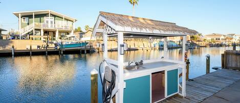 A docked boat with a small bar area, a wooden deck, and a house in the background.