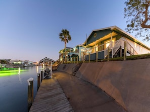 A waterfront property with a wooden dock, a covered seating area, and a building with a staircase leading to a deck. - Palm Tiki by Miss Kitty’s (Rockport)