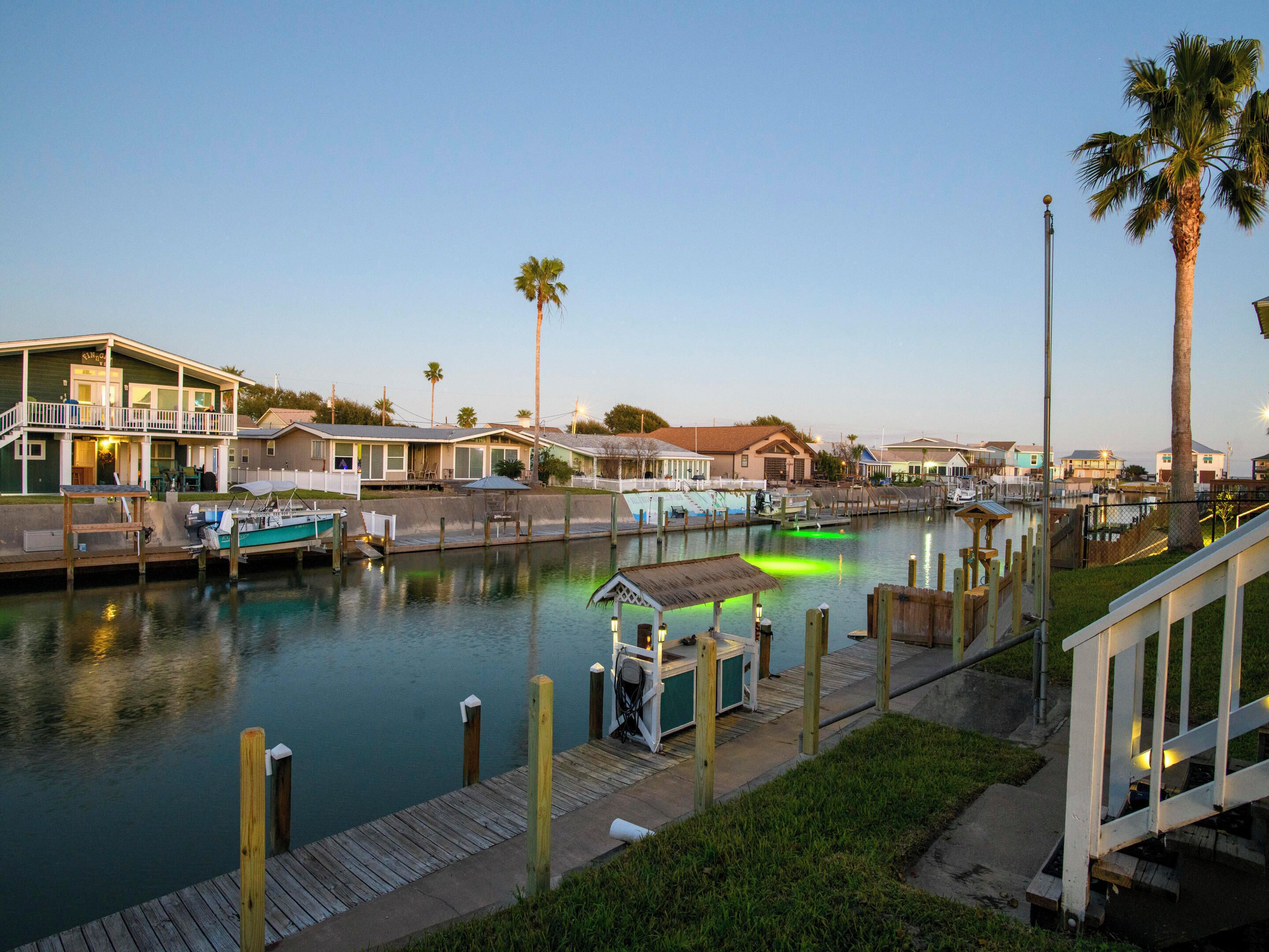 A marina with docked boats, a small dockside building, and houses along the water.