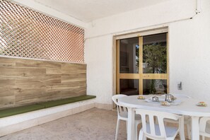 Une terrasse avec un banc en bois, une table avec des chaises et une fenêtre donnant sur un paysage verdoyant.