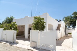 Un bâtiment blanc avec un escalier, une antenne parabolique et un portail orné d’un motif solaire.