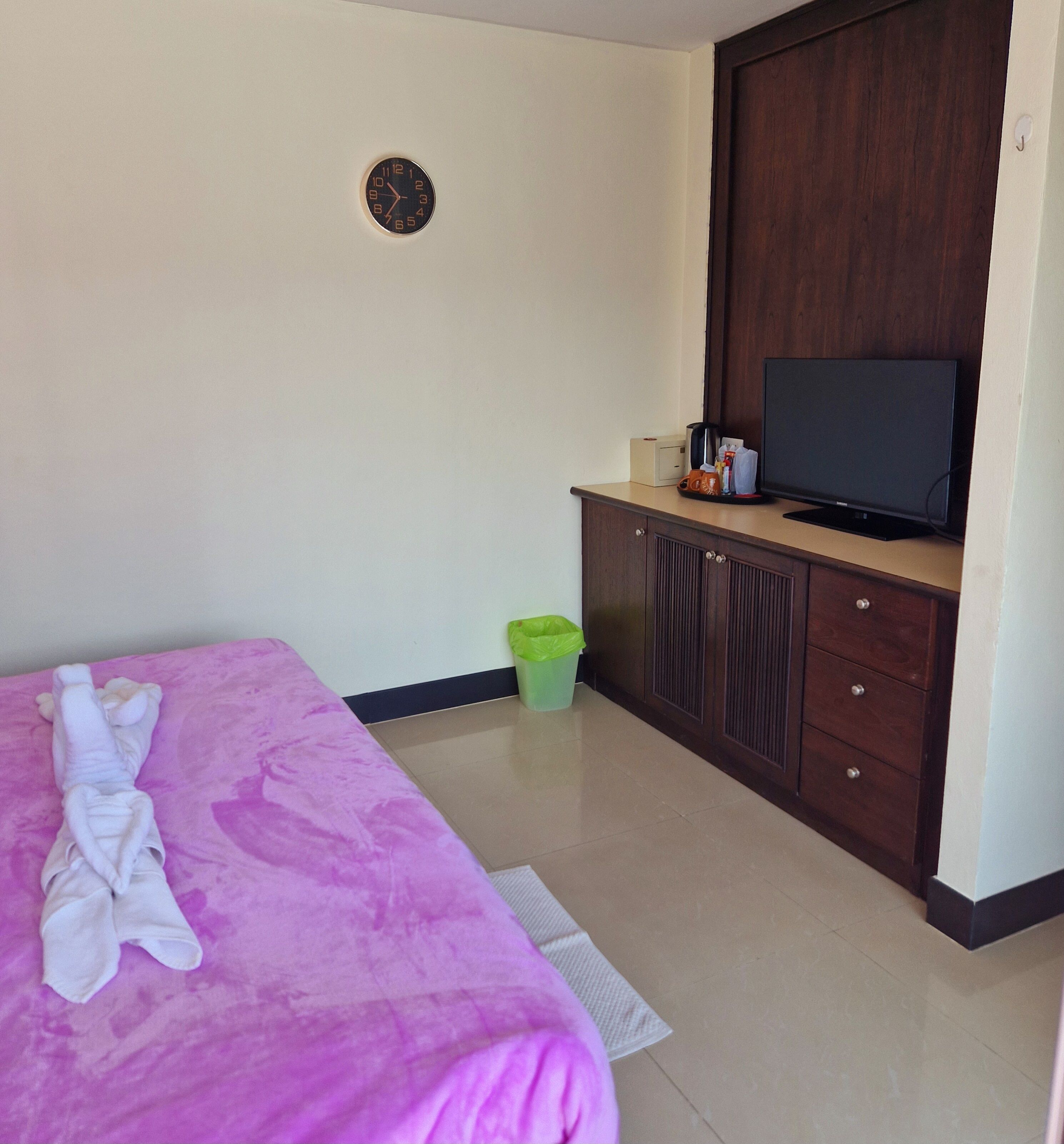 A hotel room with a bed, a television, a cabinet, and a trash bin.