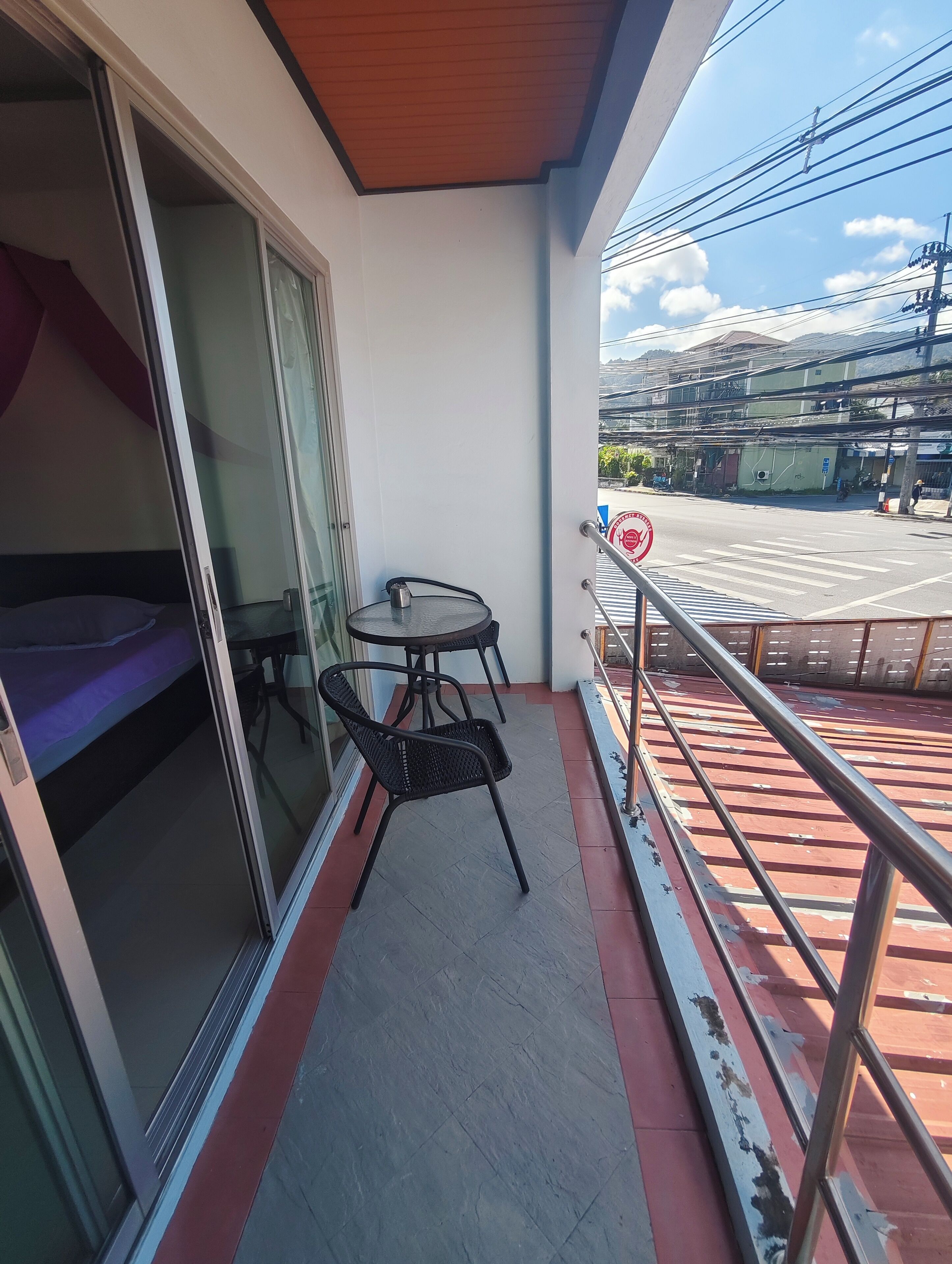 Un balcon avec une table et des chaises, un lit et une vue sur la rue et les immeubles.