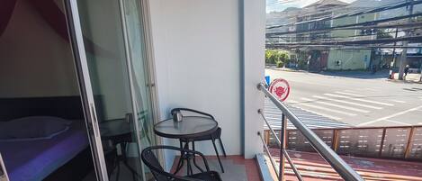 Un balcón con mesa y sillas, una cama y vistas a la calle y edificios.