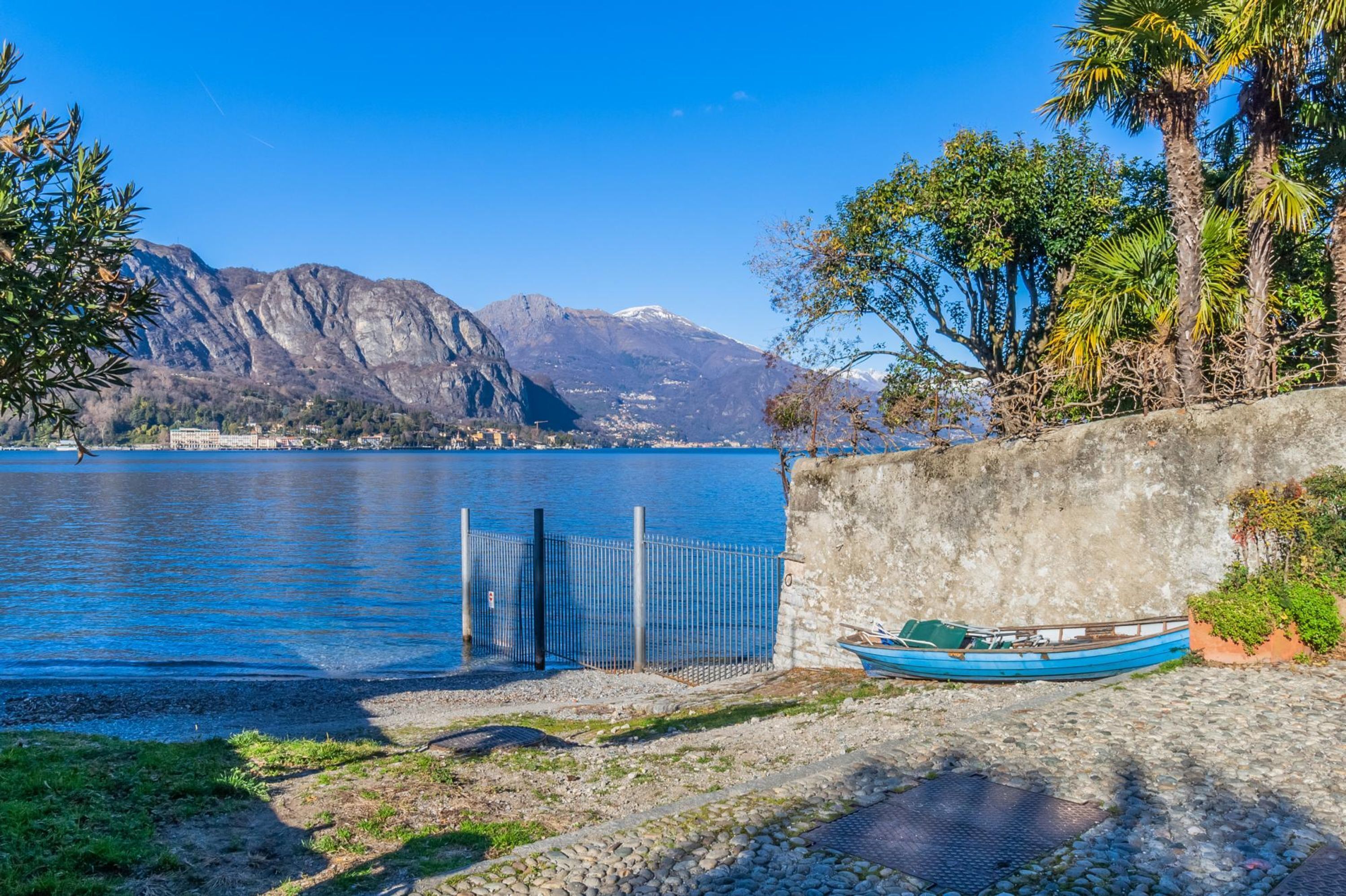 A serene lakeside view with a mountain backdrop, a dock with a boat, and a stone wall.