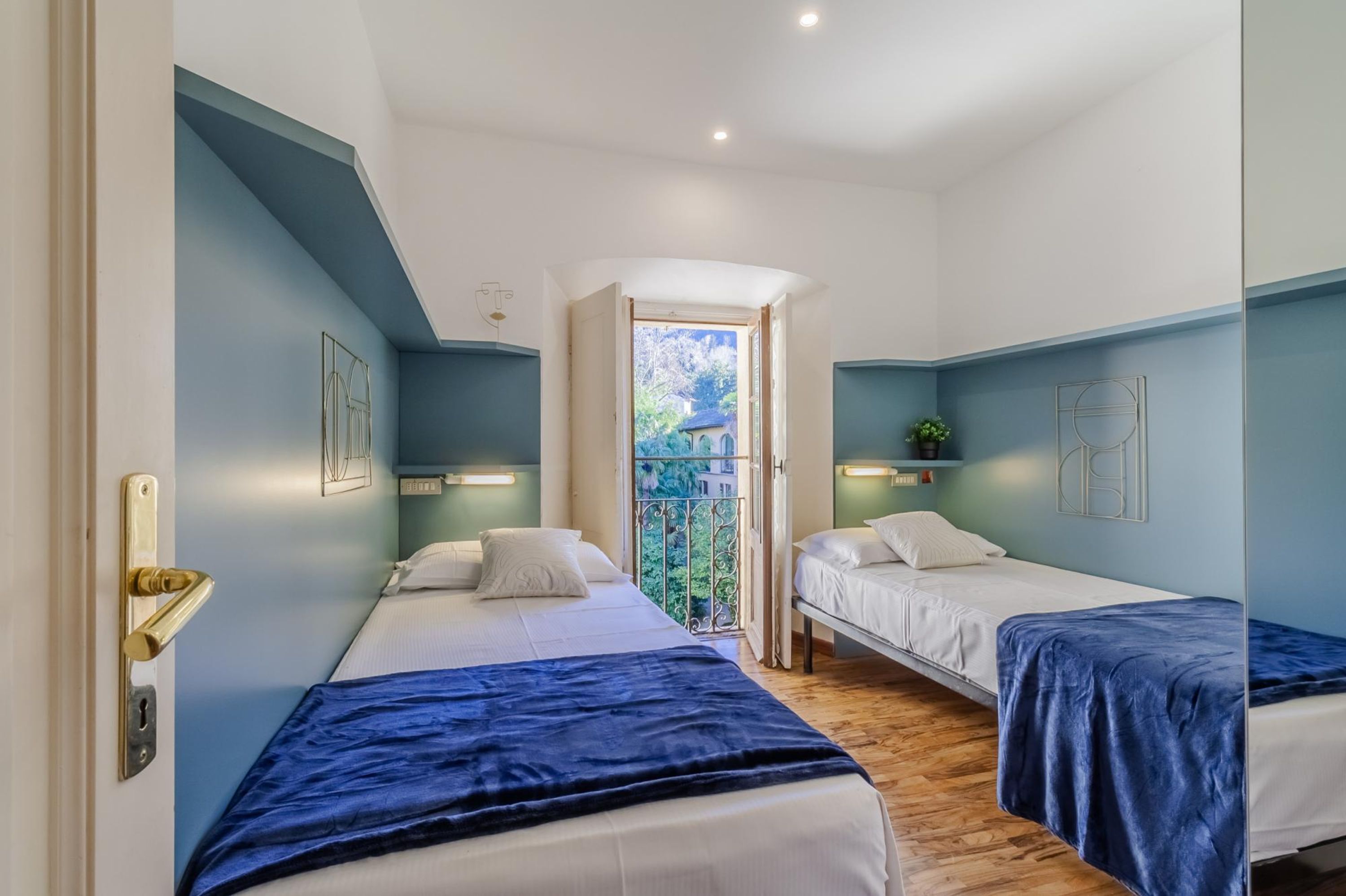 Une chambre d’hôtel avec deux lits, un balcon offrant une vue agréable et une porte dotée d’une poignée en laiton.