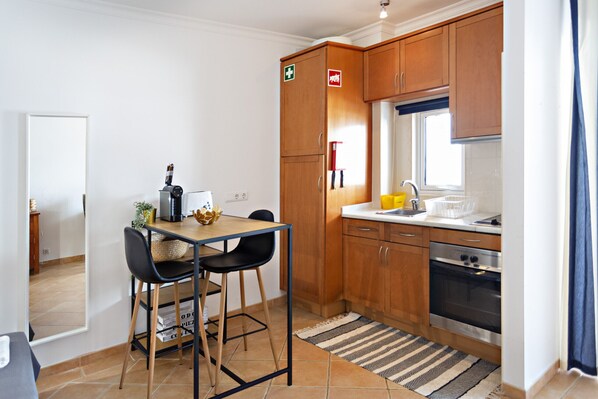 Een kleine keuken met houten kastjes, een inbouwoven en een eethoek met een tafel en stoelen.