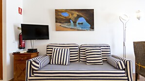 A striped sofa with pillows, a flat-screen TV, a fire extinguisher, and a painting of a boat under a rock formation.