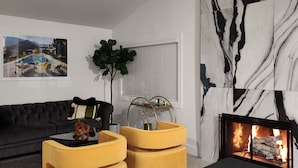 A modern living room with a black sofa, yellow ottomans, a fireplace, and a large abstract wall art piece. - PS, Love Always (Palm Springs)