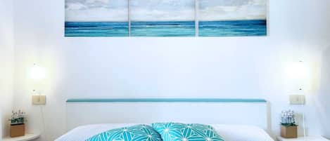 A bedroom with a bed, two nightstands, a wall-mounted shelf, and a painting of a seascape.