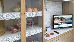 A kitchen with a wooden cabinet, a glass display case with lace, and a television on a white table.