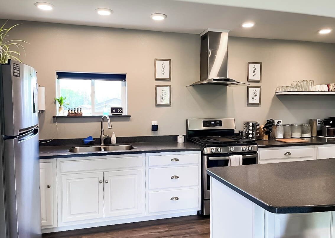A modern kitchen with white cabinets, stainless steel appliances, and a window with a view.