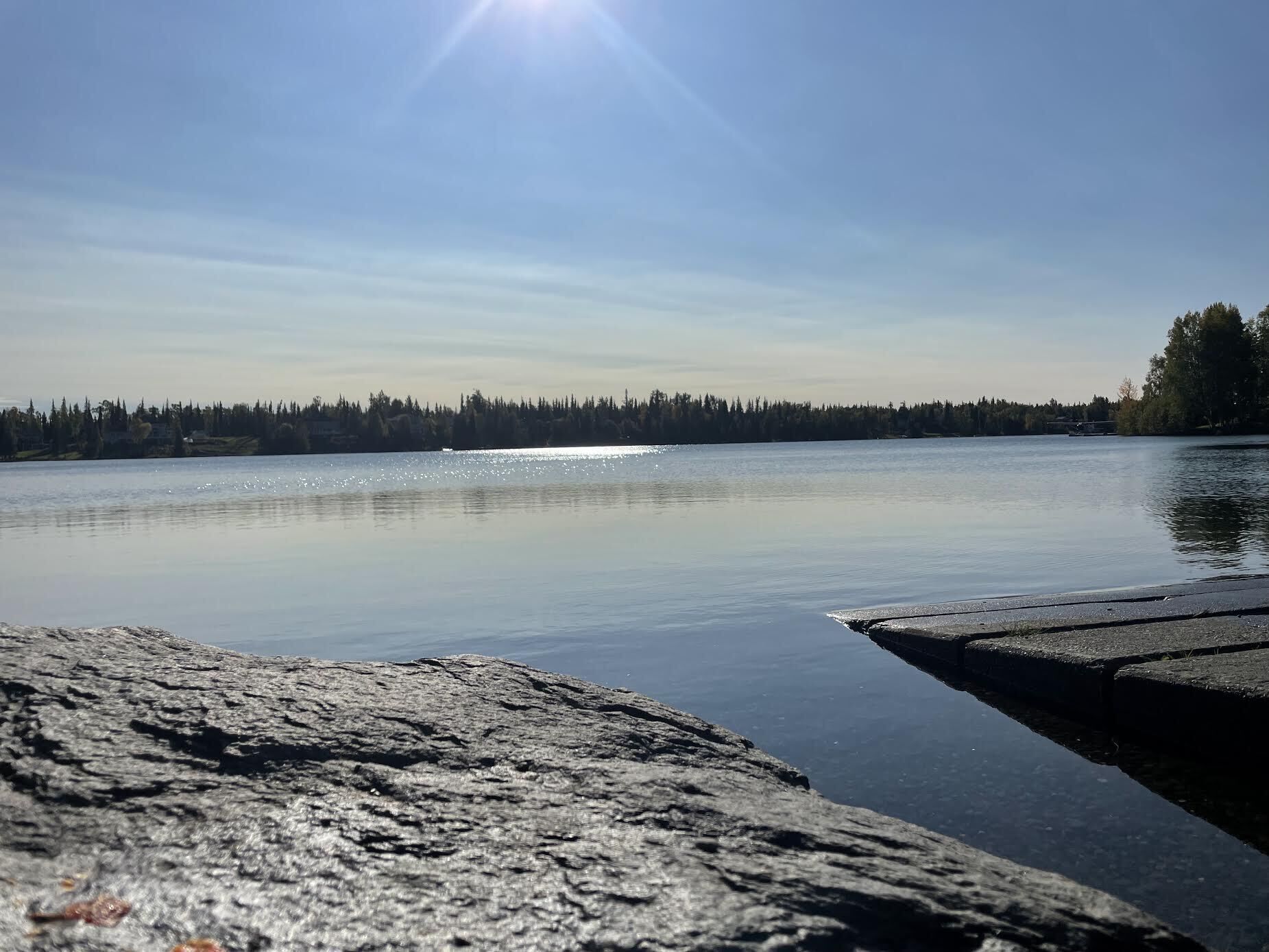 Un lac paisible, bordé d’une rive rocheuse, avec une forêt en arrière-plan.