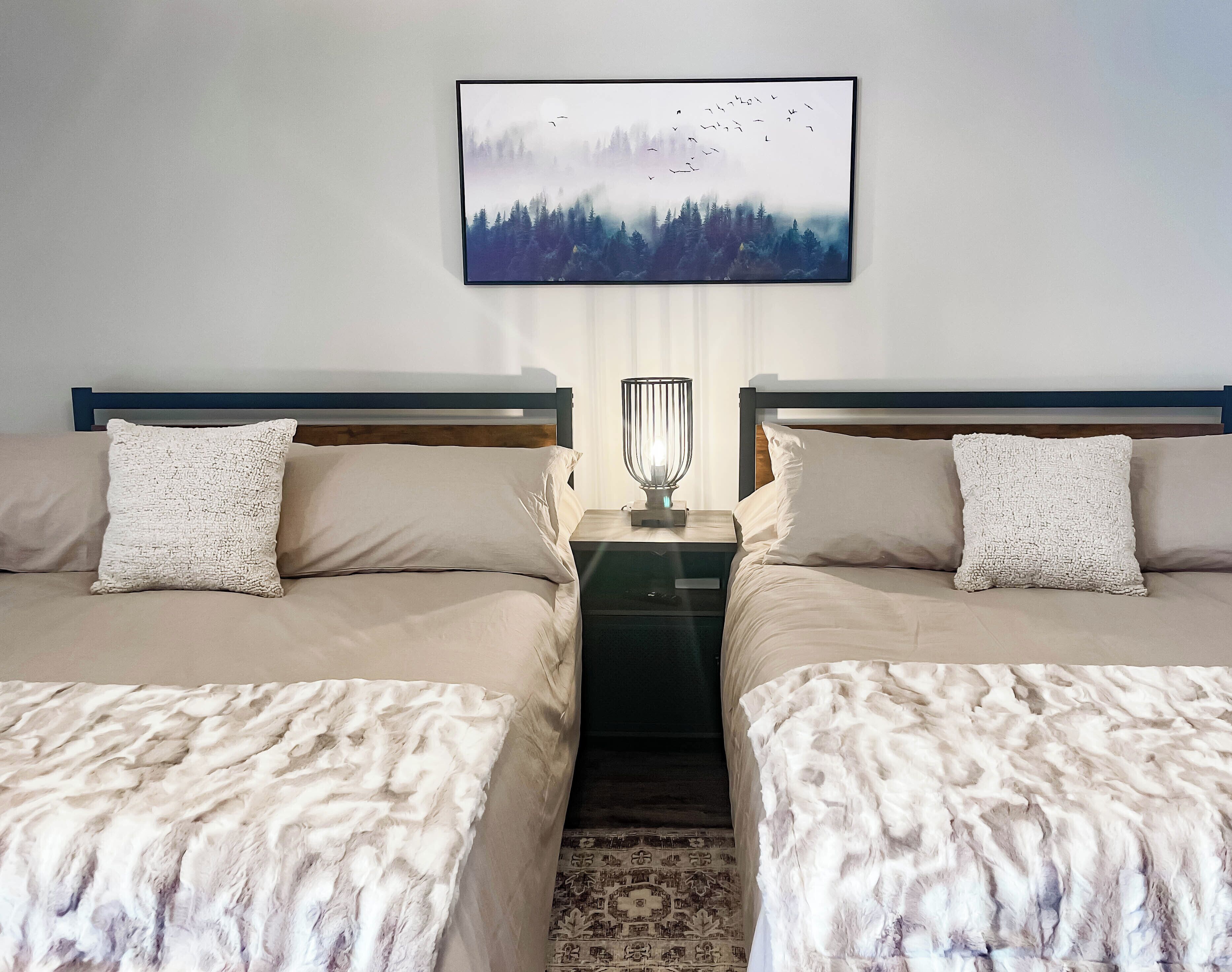 A hotel room with two beds, a nightstand with a lamp, and a framed picture on the wall.