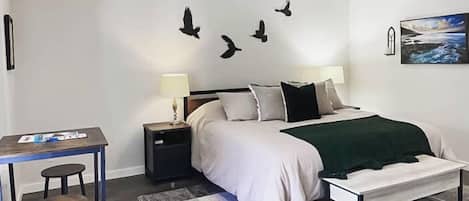 A bedroom with a bed, bedside tables, a desk, a chair, a ceiling fan, and a painting on the wall.
