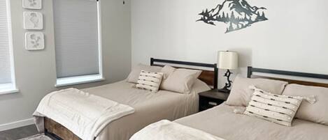 A bedroom with two beds, a ceiling fan, a window with blinds, and a wall-mounted lamp.