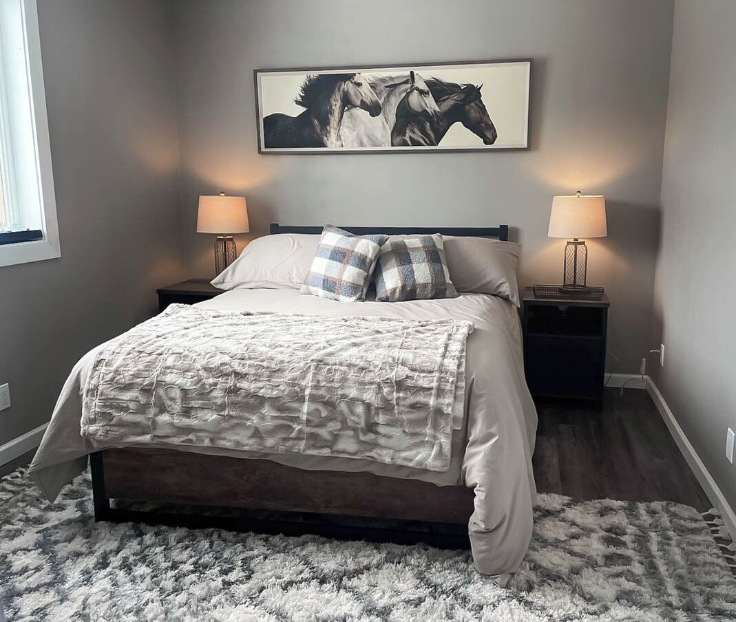 Une chambre à coucher avec un grand lit, deux tables de chevet avec des lampes, un tapis et un tableau sur le thème des chevaux accroché au mur.