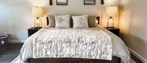 A bedroom with a large bed, two bedside tables with lamps, a rug, and two framed pictures on the wall.