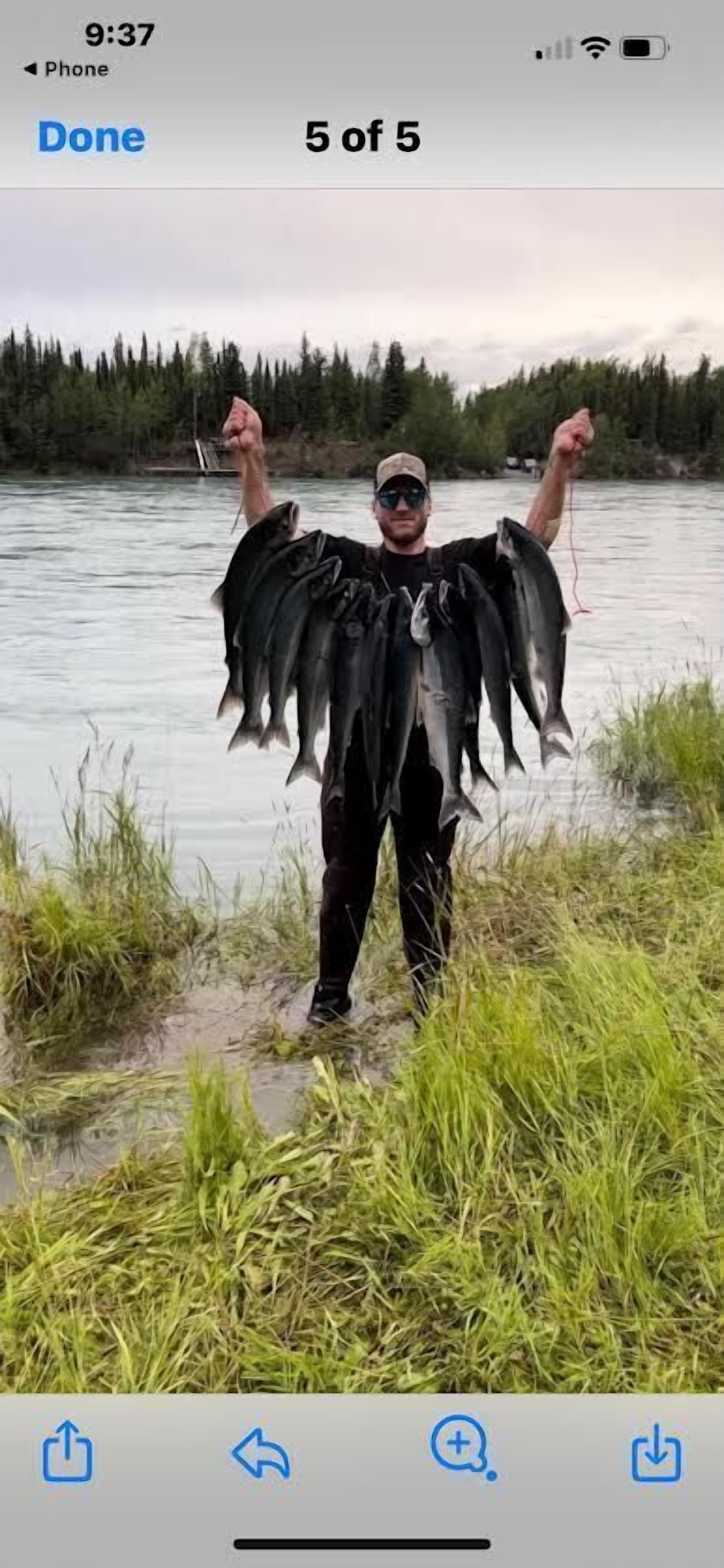 A person holding five fish by a river.