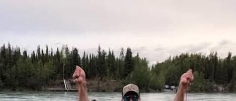 A person holding five fish by a river.