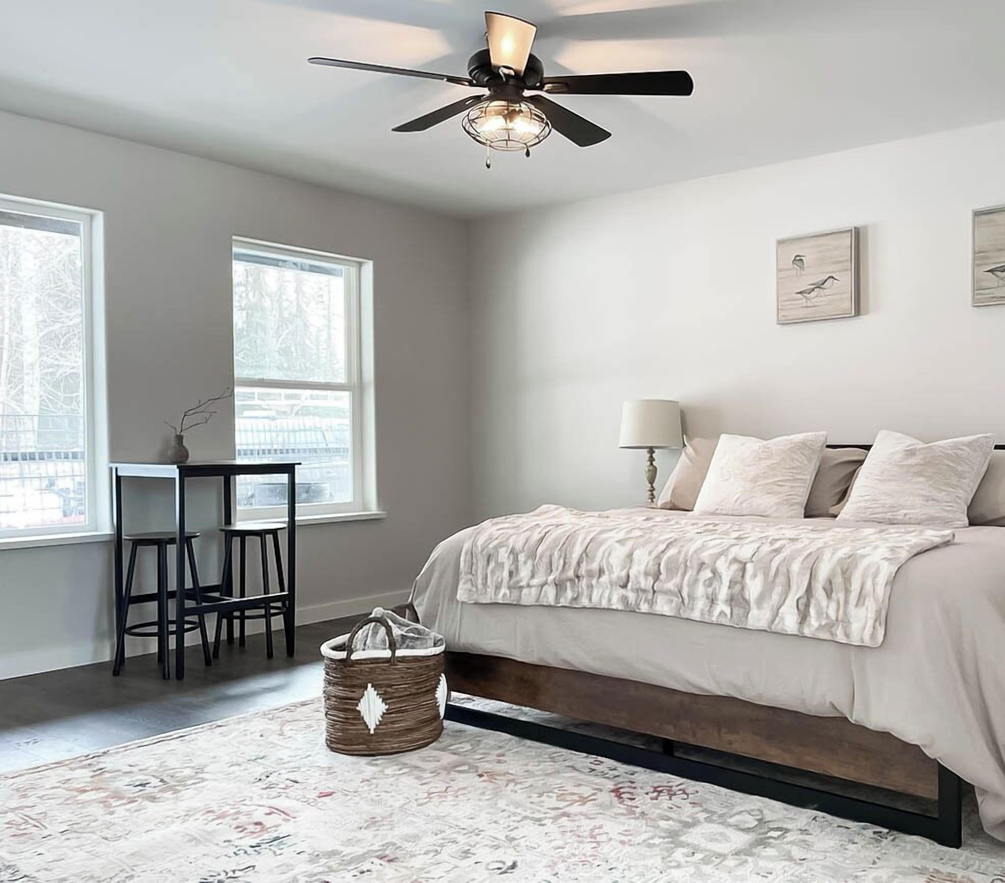 Un dormitorio con cama, escritorio, silla, lámpara y ventilador de techo.