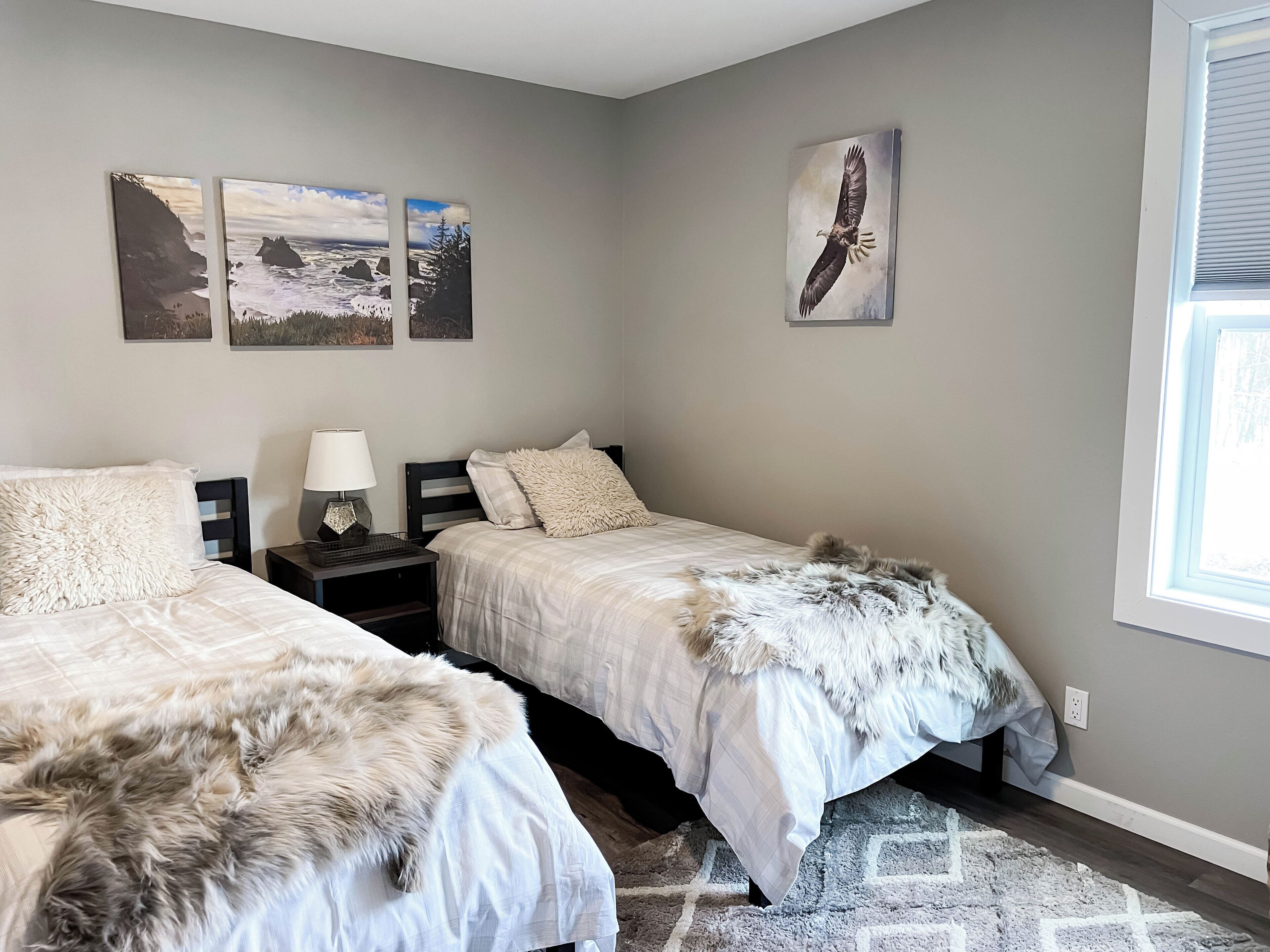 A bedroom with two beds, a nightstand, a lamp, and artwork on the wall.