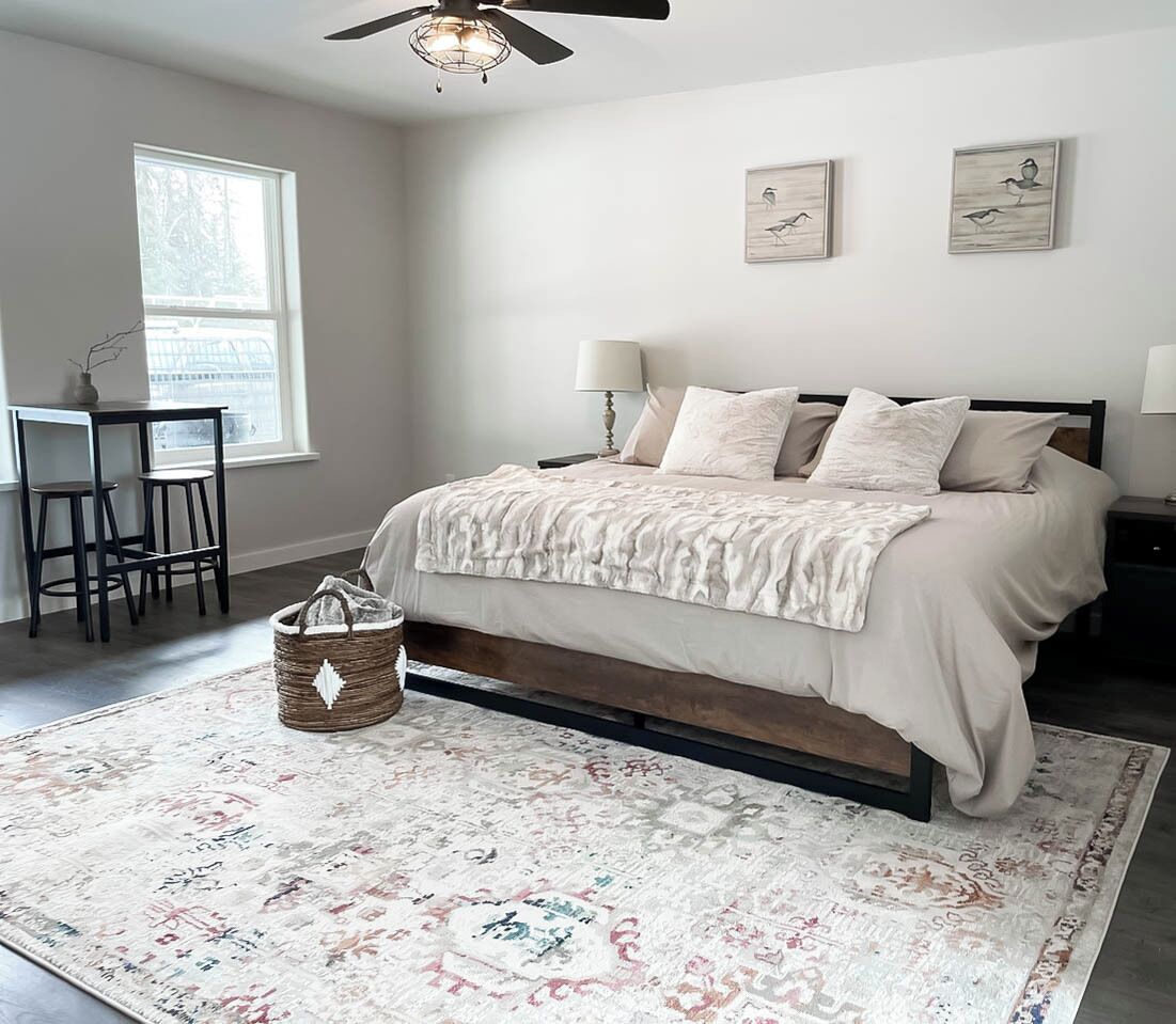 A bedroom with a bed, bedside tables, a ceiling fan, a window, and artwork on the wall.